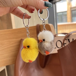 Detail of yellow and white plush duck keychains with metal chains on a brown bag