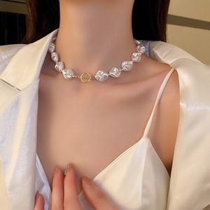 Gros plan d'un collier de perles baroques avec fermoir OT doré porté par un mannequin