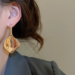 Dettaglio di orecchini a foglia d'oro oversize con finitura a specchio e drappeggio artistico
