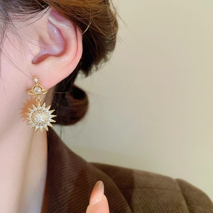 Detail view of gold planet and sun stud earrings with shimmering zircon stones
