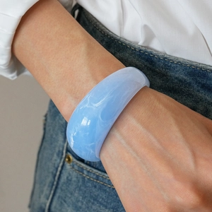 Detail of light blue resin cuff bracelet with white marble texture on a female wrist
