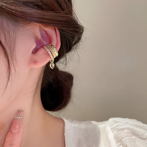 Macro detail of gold triple layer ear cuff featuring zircon heart charm on model's ear