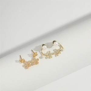 Nahaufnahme von Gold-Blumenohrringen mit Zirkonia und Perlen auf weißem Podest