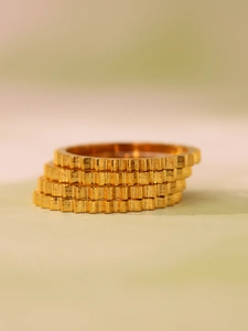 Detailed macro view of four stackable 18k gold-plated gear-edged rings with brushed metal texture