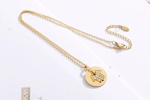 Detail of gold Hamsa Hand necklace with diamonds next to a measuring ruler