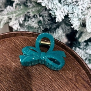 Teal bow hair claw clip displayed on a wooden tray with festive pine decor