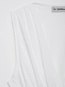 Détail d'un haut blanc sans manches avec col en V et tissu plissé texturé de haute qualité