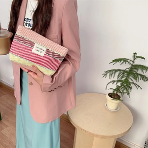 Detail of colorful striped woven clutch bag held by model featuring pink and yellow tones