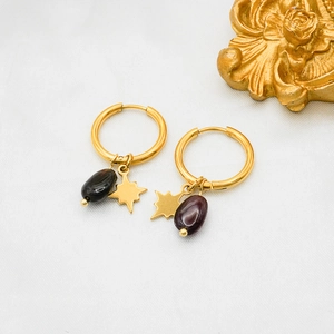 Detailed shot of gold hoop earrings with star charms and dark natural stones on white silk
