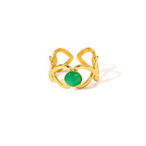 Détail d'une bague coeur dorée évidée avec une pierre précieuse verte sur fond blanc