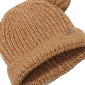 Close-up of caramel knit beanie showing maple leaf leather label and ribbed texture