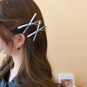 Y2K silver metallic leather bow hair clips worn on side of wavy dark brown hair