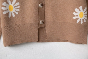 Detail of brown knit cardigan hem featuring daisy embroidery and amber-style buttons