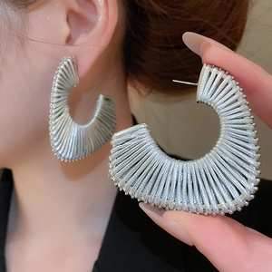 Close-up detail of silver-toned braided C-shaped hoop earrings with woven metallic texture