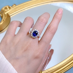 Classic oval blue sapphire ring with halo zircon setting shown on a finger