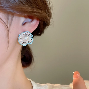 Close-up of a hollow flower earring with pearl and blue enamel on a model ear