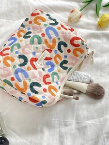 Detailed view of floral quilted cotton makeup bag with brushes on white bedsheet