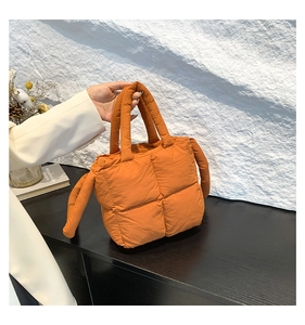 Detailed view of orange quilted puffer bag with puffy texture and shoulder strap