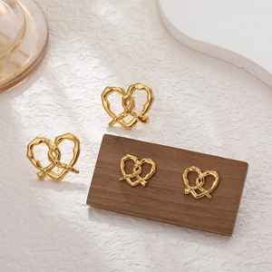 Detailed view of 18K gold pretzel-shaped stud earrings on a minimalist wooden stand