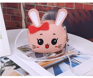 Detail of pink PU leather bunny crossbody bag with red bow and white woven strap