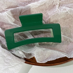 Detail view of large emerald green geometric hollow hair claw clip on white textured paper