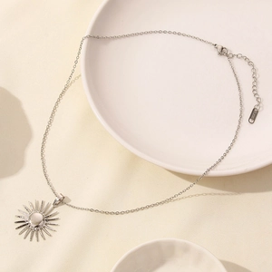 Dettaglio della collana con ciondolo a sole in acciaio inox su piatto ceramica