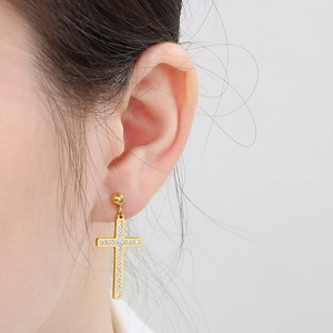 Close-up of golden cross earrings with zircon crystals on a person's ear lobe