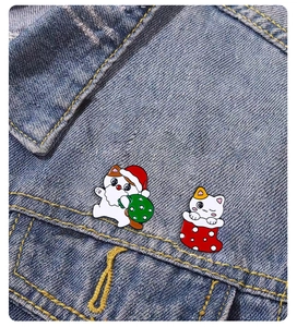 Detail of cute Christmas cat enamel pins on denim jacket featuring a stocking and gift bag