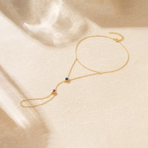 Detail of gold finger bracelet featuring red and blue round stones on elegant stone texture