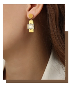 Macro view of gold plated square pendant earrings with white pearl inlay and crystals
