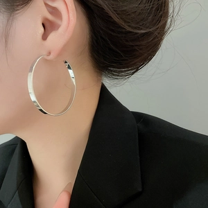 Side view of large silver hoop earring with polished metallic finish on female model