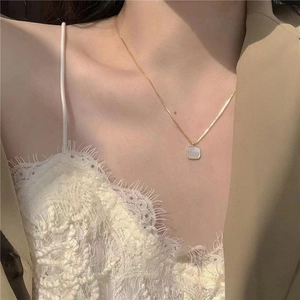 Close-up of a minimalist gold chain necklace with a square white mother of pearl pendant