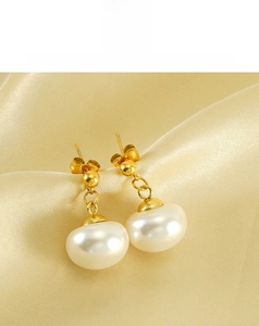 Detail view of elegant gold pearl drop earrings on champagne silk background