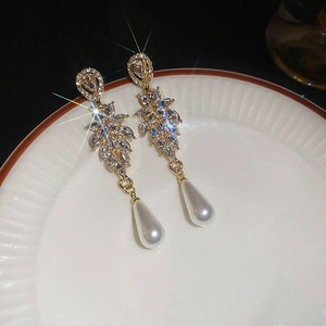 Detailed view of leaf-shaped crystal earrings with large teardrop pearl on white ceramic