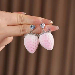 Close-up of pink velvet strawberry earrings with a clear heart-shaped gemstone stud