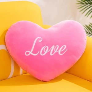 Nahaufnahme eines rosa Plüsch-Herz-Kissens mit weißer Love-Stickerei auf einem Sofa