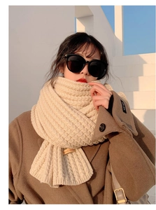 Detailed view of beige cable-knit scarf texture with a handmade leather label detail