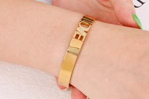 Detailed macro view of a gold-colored steel bangle featuring LOVE lettering with crystal inlay