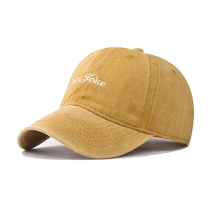 Detailed close-up of NO JOKE embroidery on a mustard yellow washed cotton baseball cap