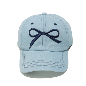 Detail of light blue denim baseball cap featuring dark blue bow embroidery and dual stitching