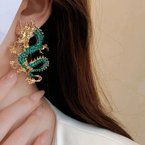 Dettaglio di un orecchino a forma di drago dorato con strass verdi scintillanti sul modello