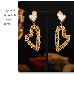 Detail of golden double heart earrings with white mother-of-pearl and textured finish