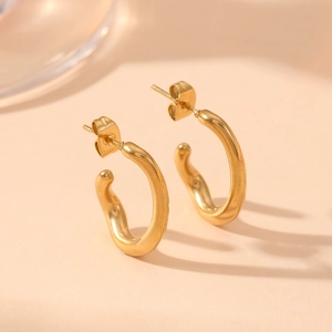 Pair of minimalist golden C-shaped twisted earrings in stainless steel on a warm background