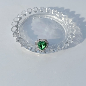 Detail of heart-shaped green crystal ring with pavé stones on a glass tray