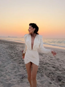 Detail of white satin mini dress with deep V-neck and long sleeves at sunset beach
