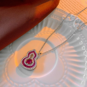 Détail d'un collier en forme de gourde avec pierre rouge et cristaux blancs sur une assiette