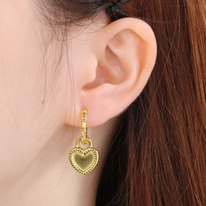 Détail d'une boucle d'oreille cœur avec bord perlé portée pour l'échelle visuelle