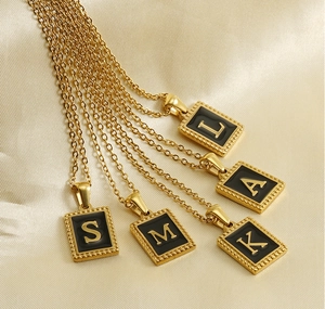 Detail of square black enamel initial pendants on 18K gold plated stainless steel chains
