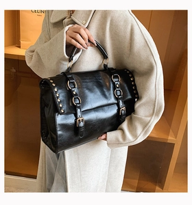Detail of black vintage satchel with gold studs and metal ring buckle on beige coat