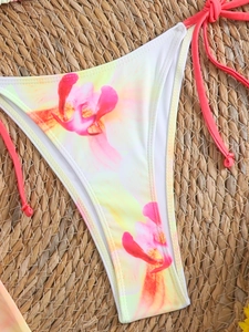 Detailed flat lay of bikini bottoms with pink floral print on natural woven mat background